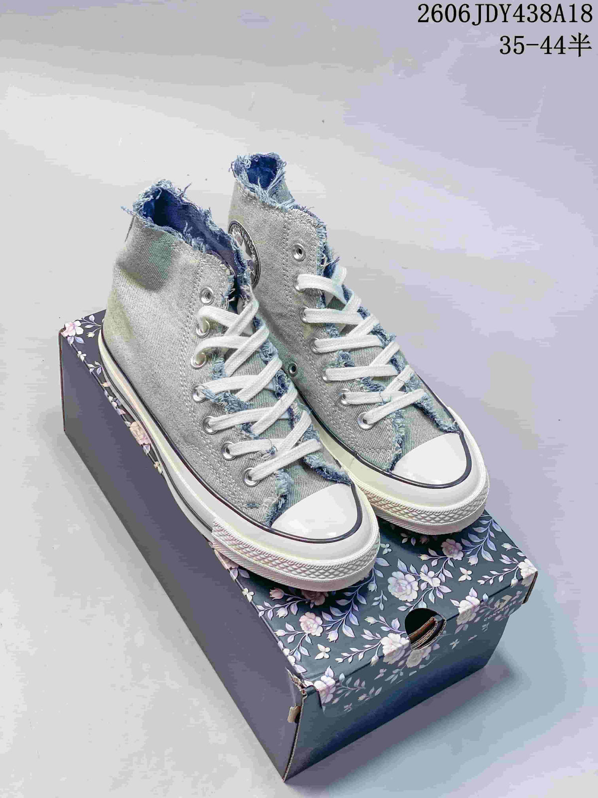 Pair of washed light blue denim high-top sneakers with white laces on a floral-patterned box