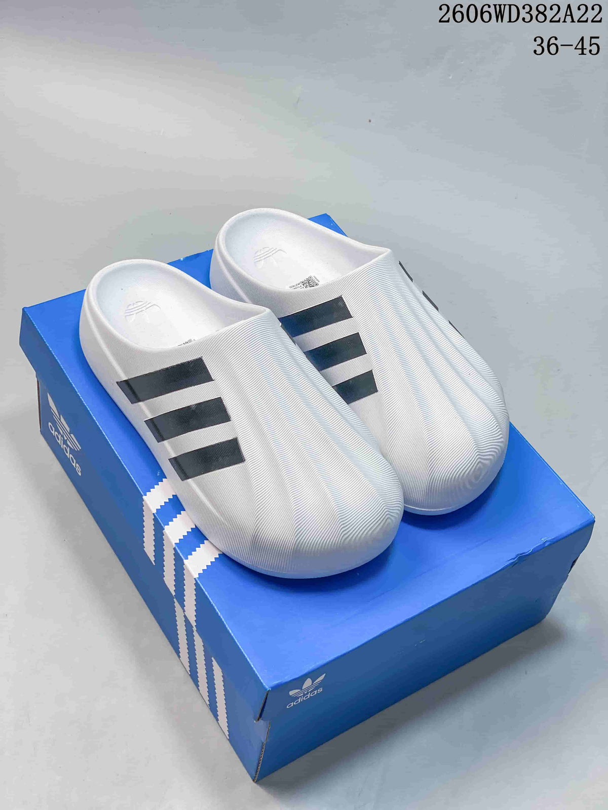 Pair of white Adidas Adifom Superstar slides with black stripes, shown on a blue shoe box