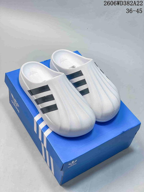 Pair of white Adidas Adifom Superstar slides with black stripes, shown on a blue shoe box