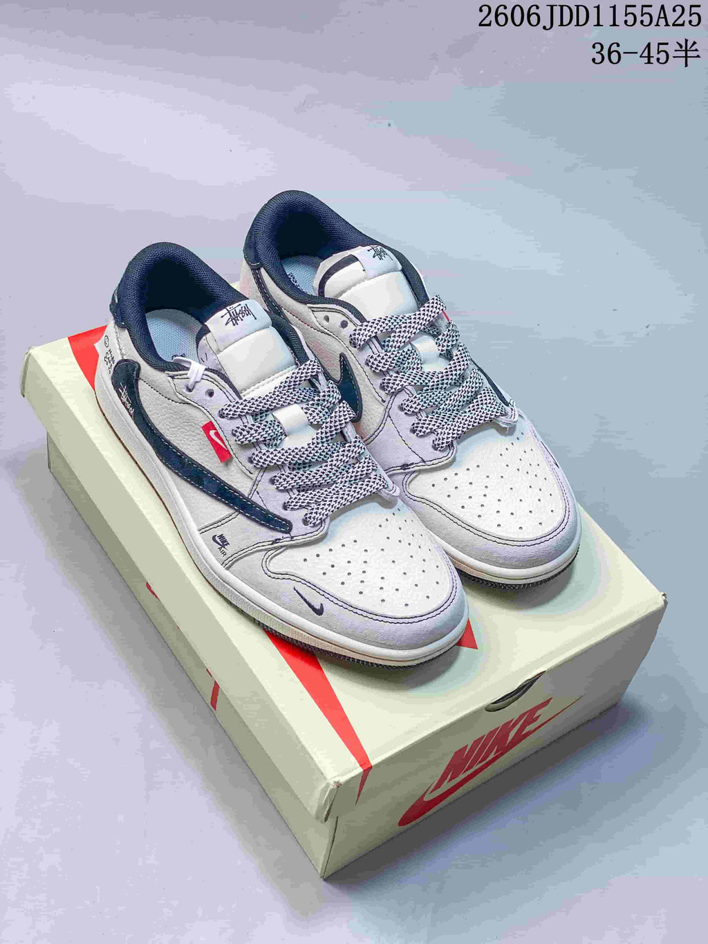 Pair of white low-top sneakers with dark blue side accents and patterned laces, displayed on a light-colored box.