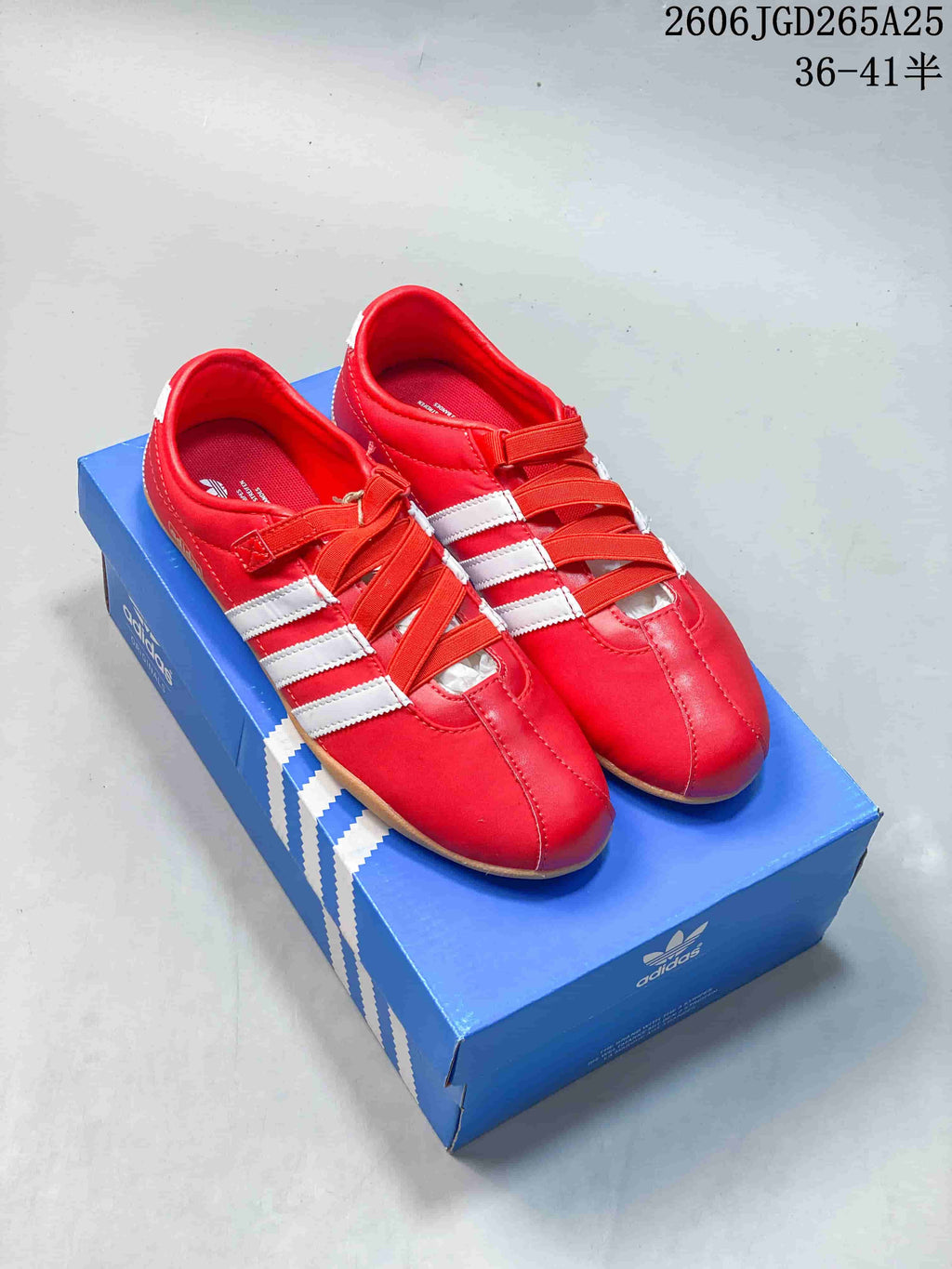 Red Adidas Tokyo W sneakers with white stripes and crossing bands, shown on a blue shoe box.
