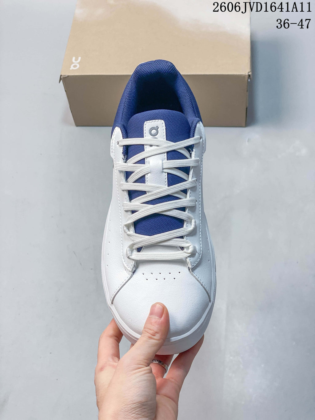 Top view of a white sneaker with blue tongue, white laces, and perforated toe.
