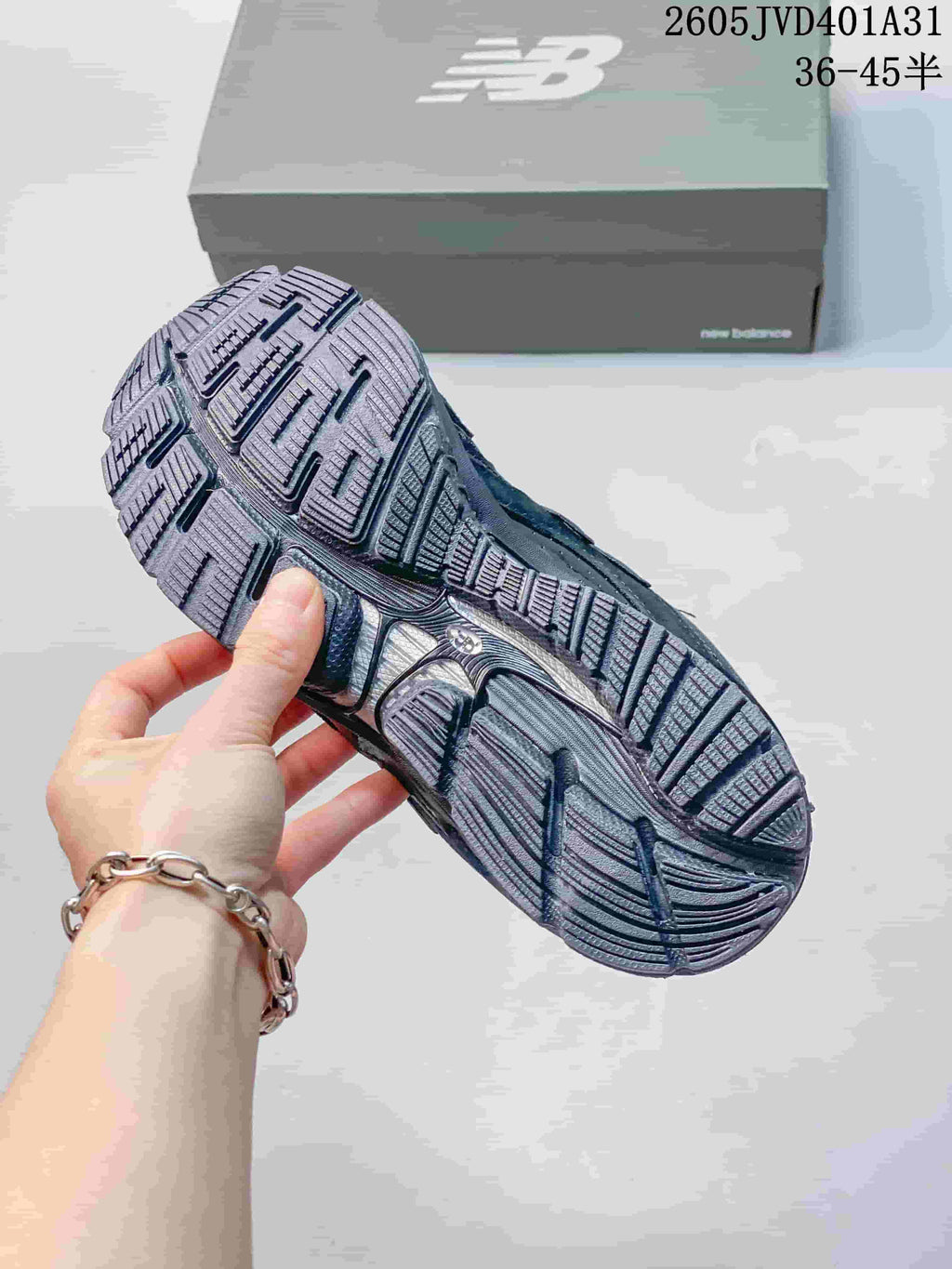 Underside of a charcoal gray New Balance sneaker showing segmented tread; size range text appears in the image.