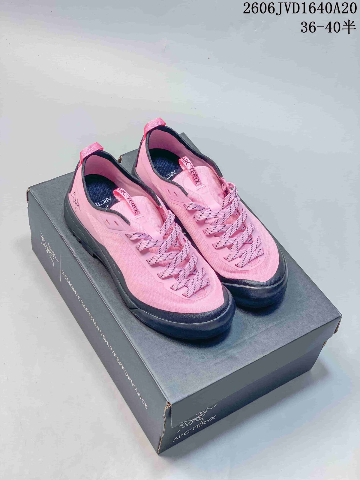 Pair of pink Arc'teryx-branded trail shoes with dark gray trim on a shoe box