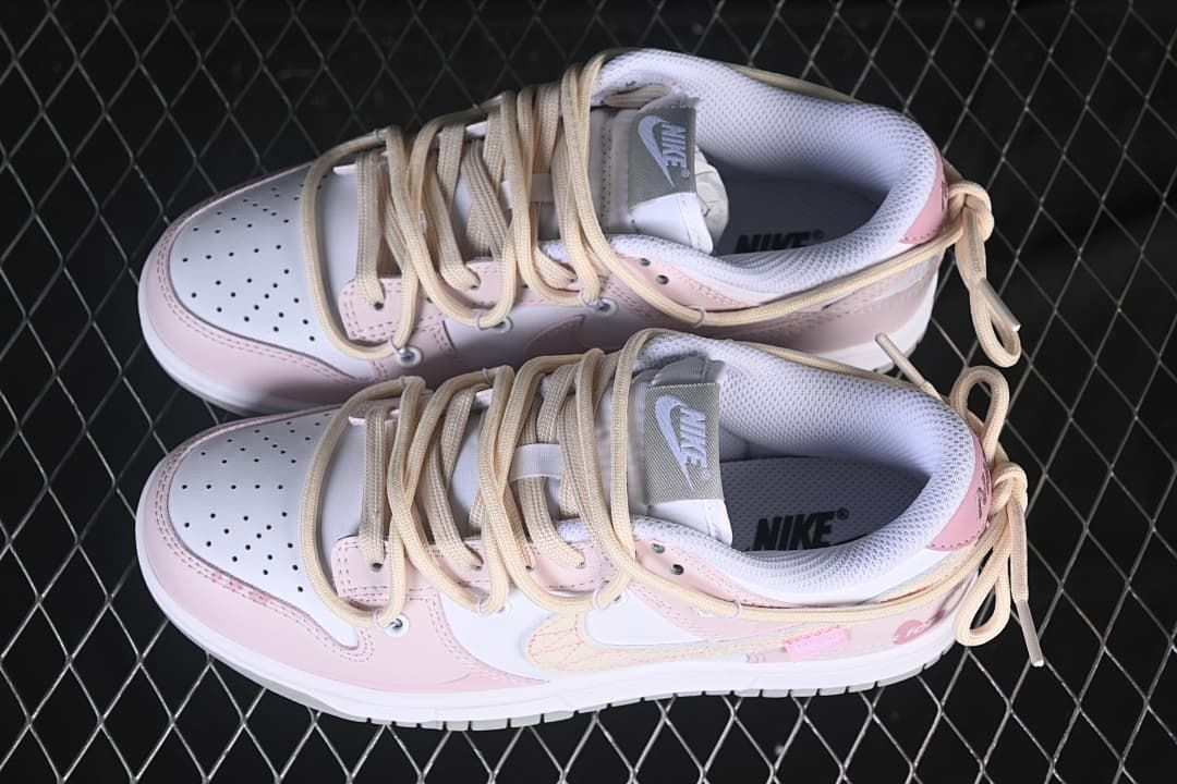 Top view of a pair of pink and white Nike SB Dunk Low sneakers showing perforated toes and cream laces