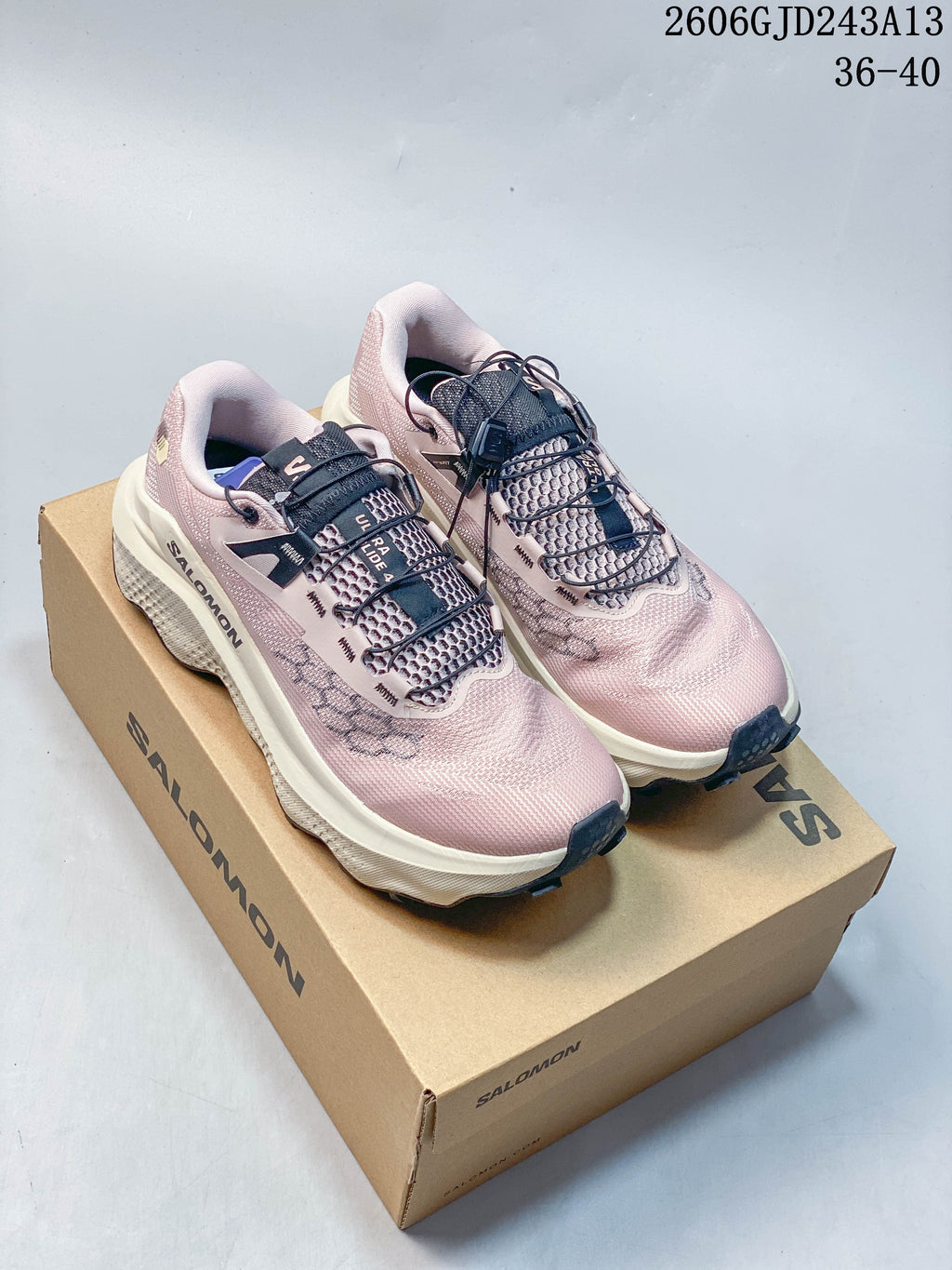 Pair of pink Salomon Ultra Glide 4 trail running shoes with dark quick-lace details on a branded box.
