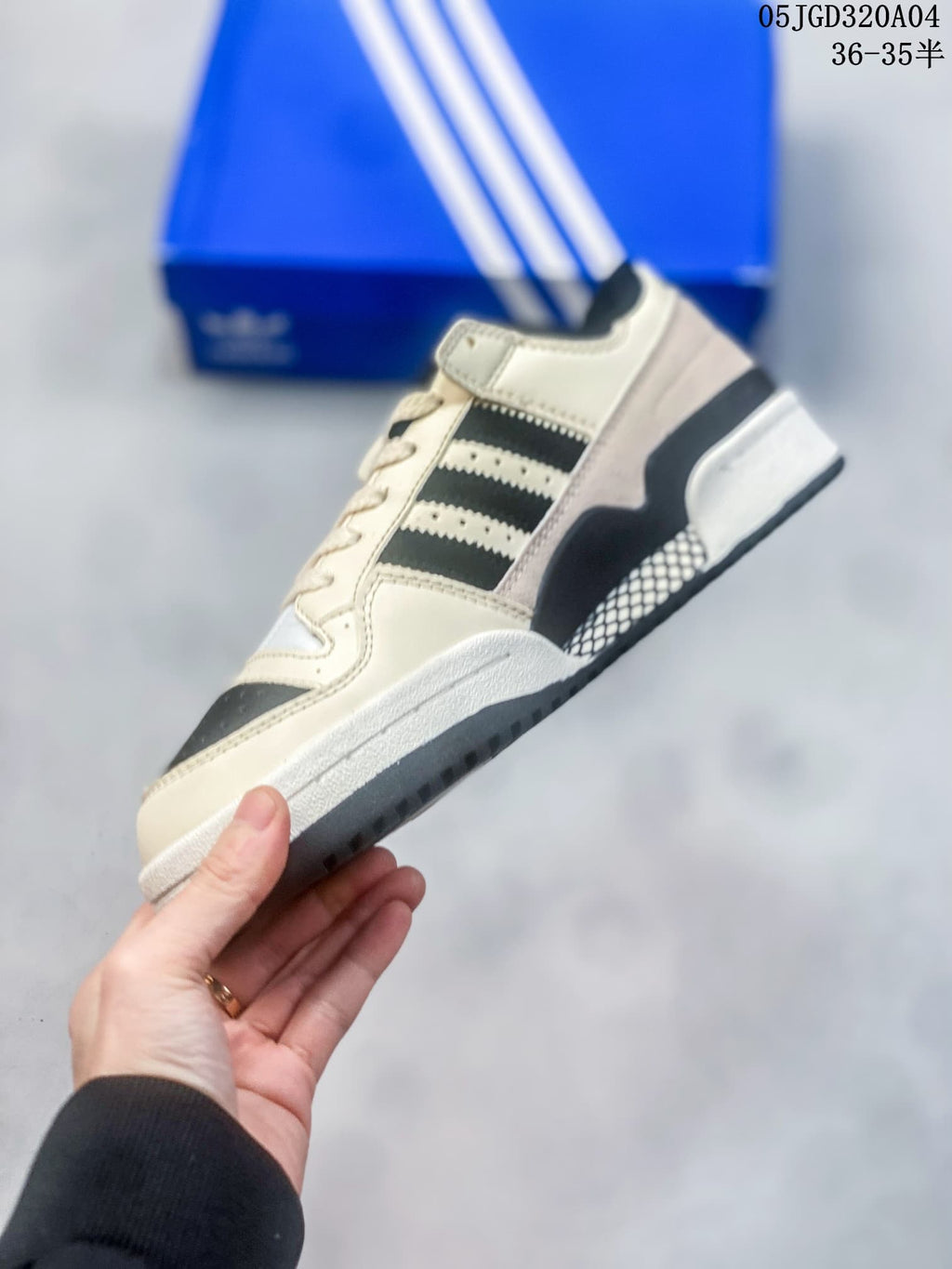 Side view of a cream and black low-top sneaker with three stripes and a hook-and-loop ankle strap.
