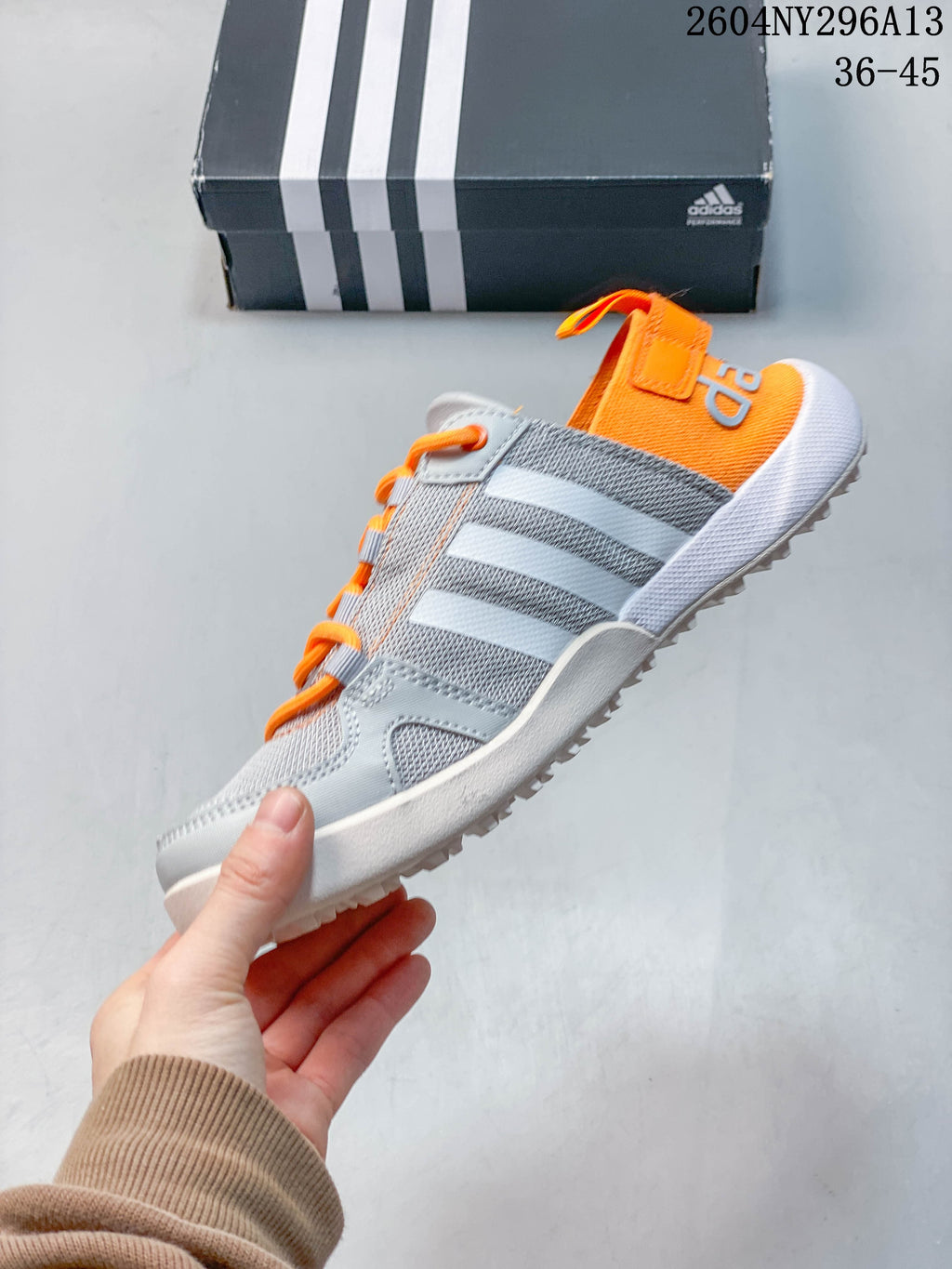 Side profile showing the grey upper, white stripes, orange laces and heel panel.