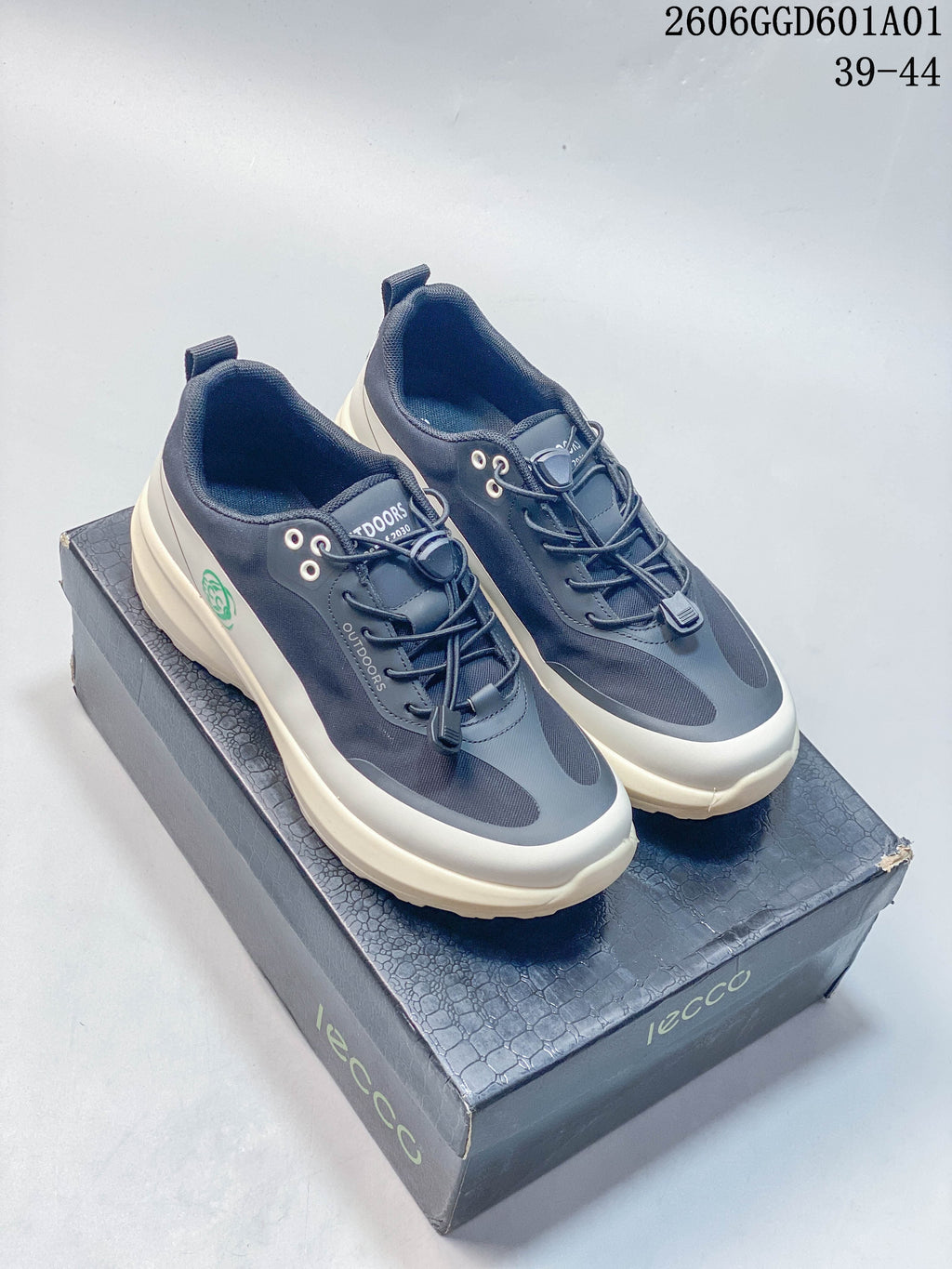 Pair of navy and grey ECCO sneakers with off-white soles shown on a shoe box