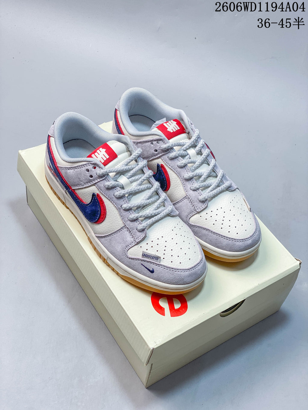 Pair of white and light grey low-top sneakers with blue and red Swoosh accents on a box