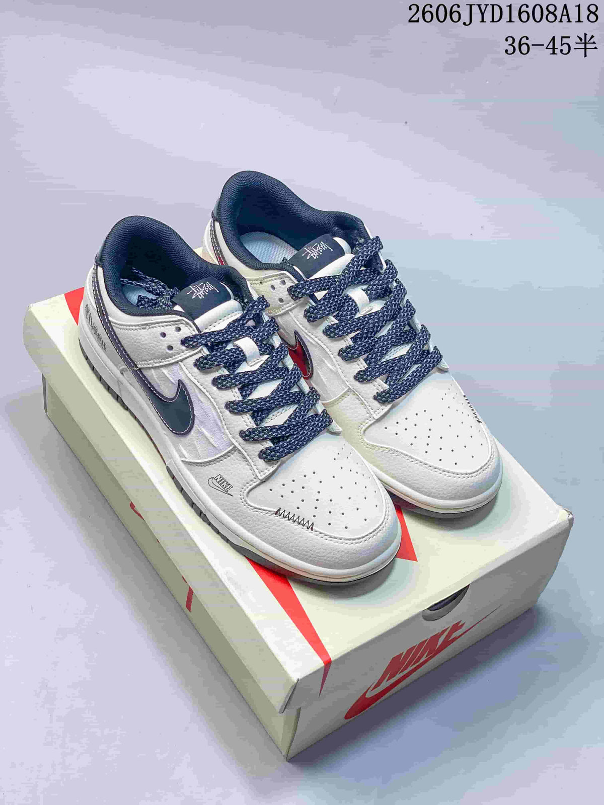 Pair of white and navy Nike SB Dunk Low sneakers with patterned laces on a box