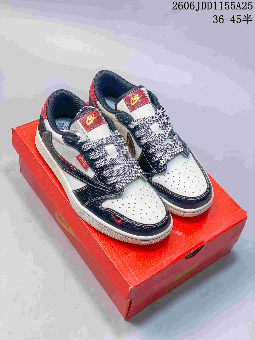 Pair of white and navy low-top Jordan sneakers with red accents on a red shoebox
