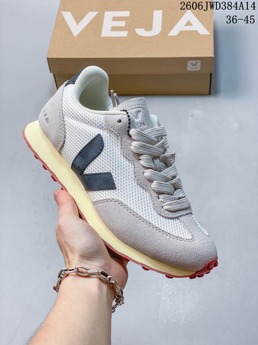 White and light-gray Veja sneaker with a dark V-shaped side logo, cream-colored midsole, and red outsole accents.
