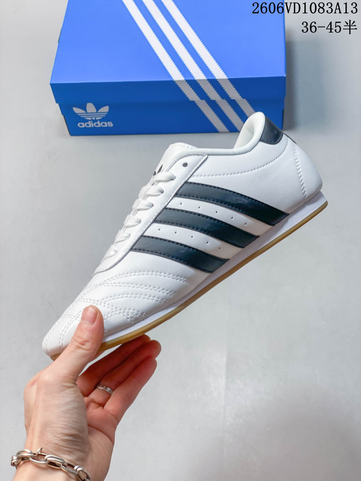 Side profile of a white Taekwondo sneaker with dark stripes and a gum-colored outsole