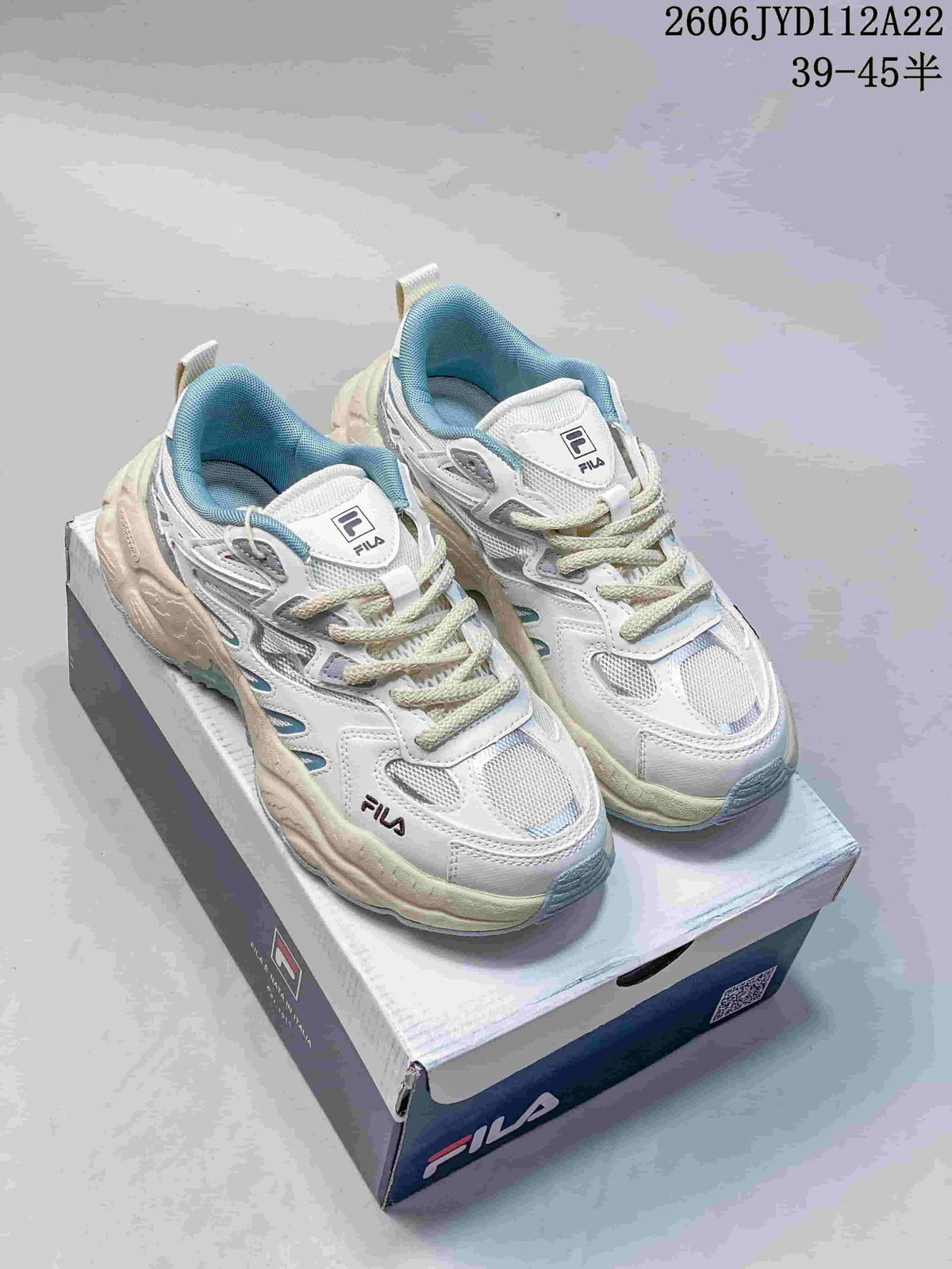 Pair of white and light blue FILA retro sneakers with cream-colored soles on a shoebox.
