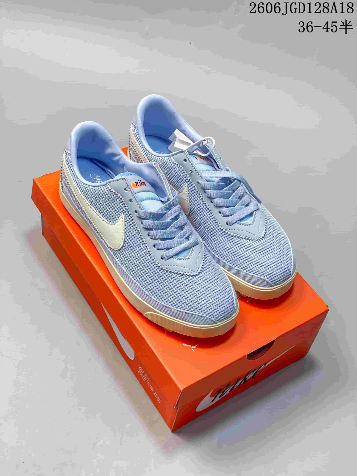 Pale blue Nike Astrograbber sneakers with light-colored side Swooshes and contrasting soles, shown on an orange shoebox.