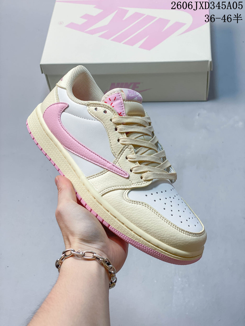 Side view of a cream and white low-top sneaker with a pink side overlay, held in front of a shoe box.