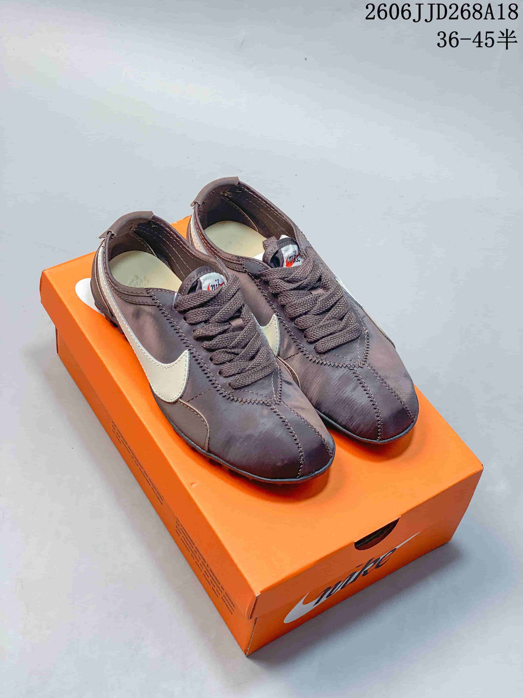 Pair of brown Nike Moon Shoe OG Summit low-top sneakers with light-colored Swooshes, shown on an orange box.