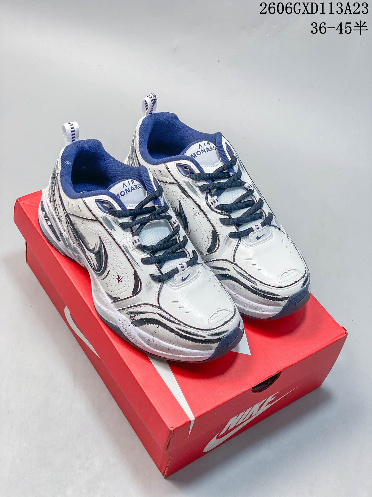 Pair of silver and white Nike Air Monarch sneakers with navy accents, shown from the front