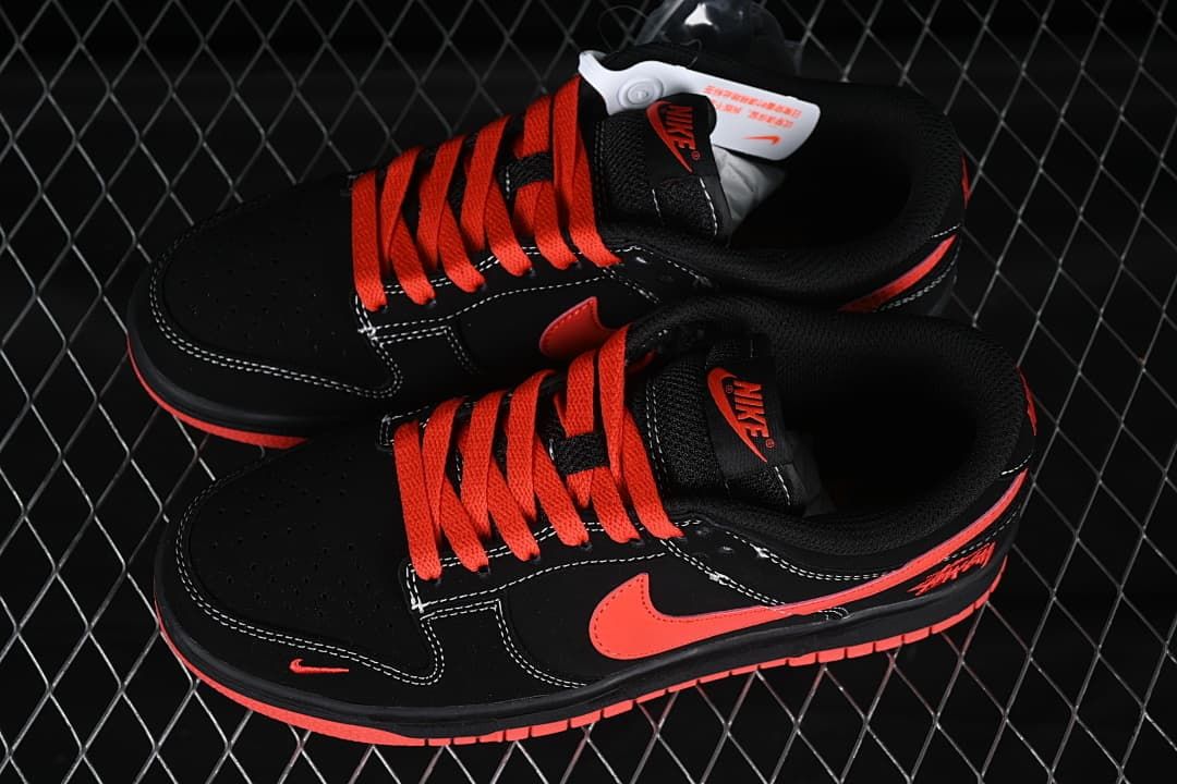 Top and angled views of a black low-top sneaker with red-orange laces, perforated toe panels, and contrasting stitching.
