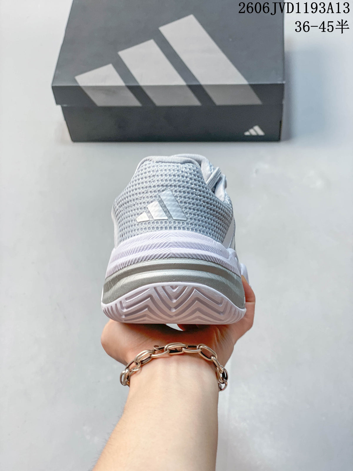 Rear view showing the heel and outsole of a white and silver Adidas tennis shoe