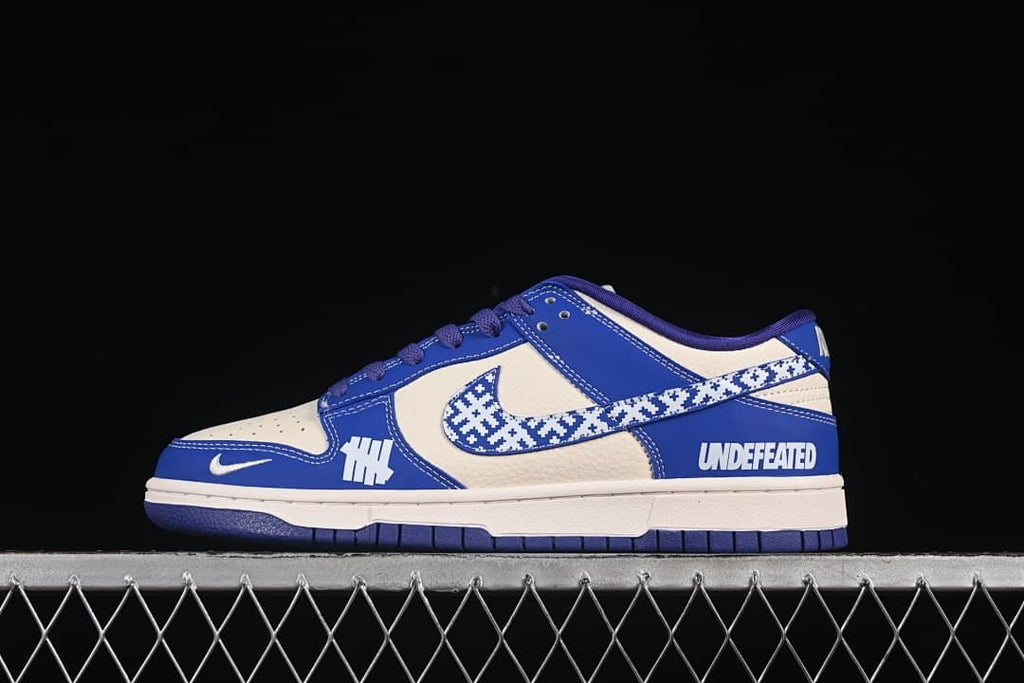 Side view of a blue and off-white Nike SB Dunk Low with a patterned Swoosh and contrasting side graphics.