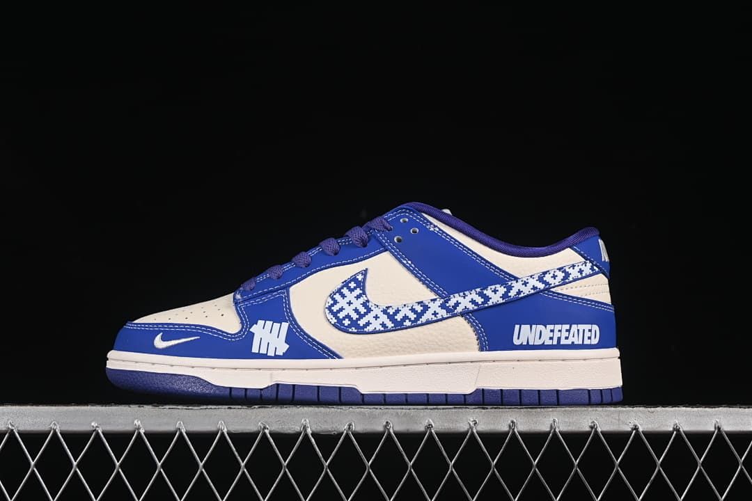 Side view of a blue and off-white Nike SB Dunk Low with a patterned Swoosh and contrasting side graphics.
