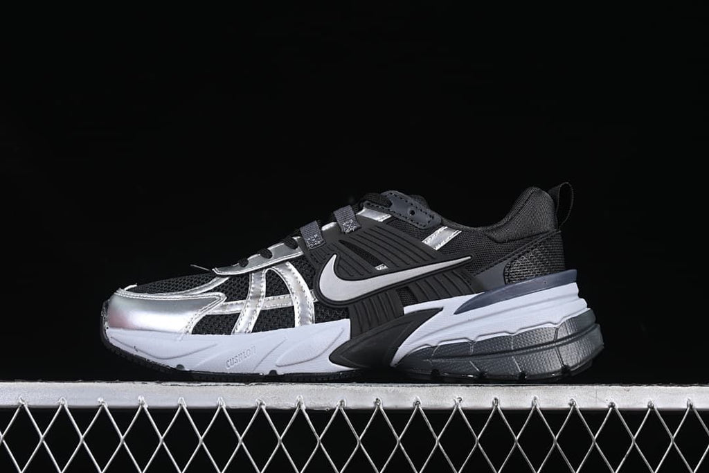 Side view of black, silver, and white Nike V2K Run shoes against a dark background