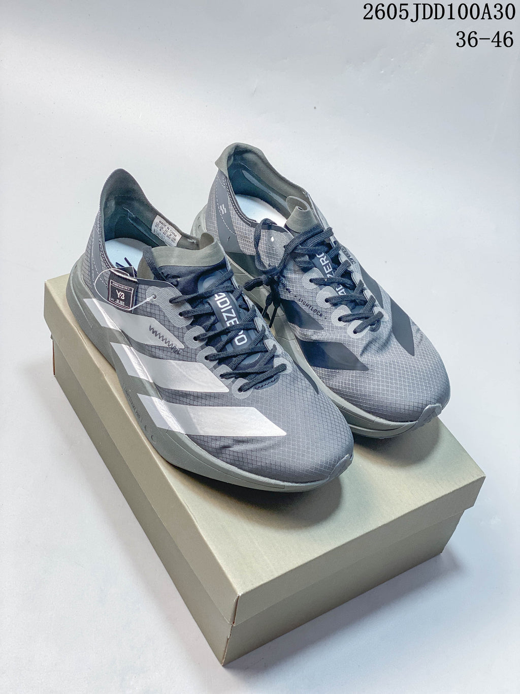Pair of gray Adidas Adizero Adios Pro 4 shoes with silver-tone stripes, shown on a box.