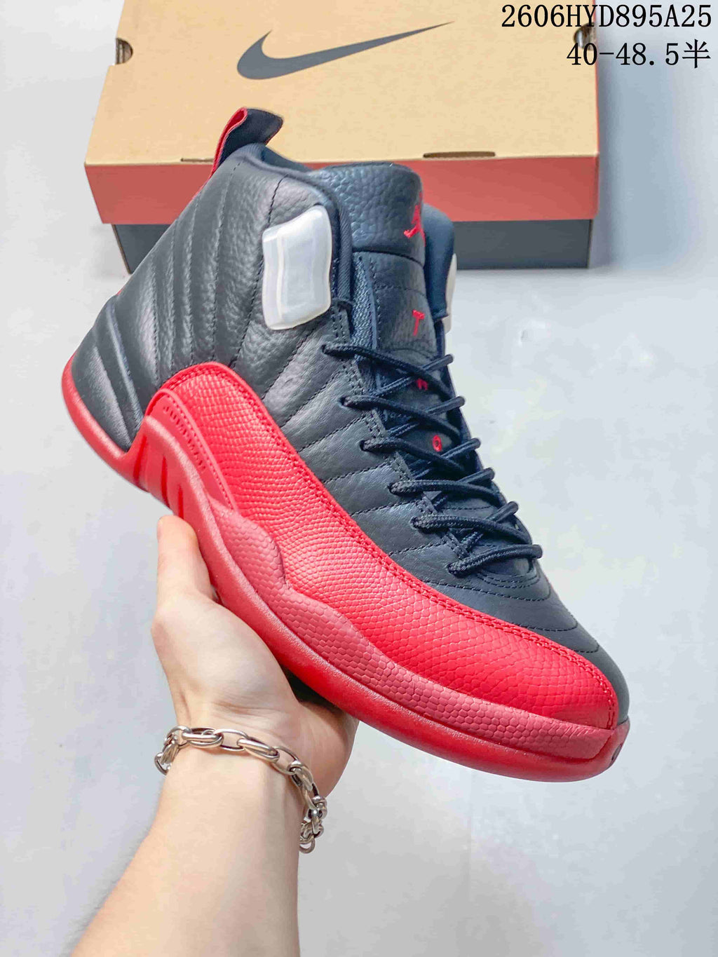 Side view of a black and red Jordan Air Jordan 12 high-top shoe, showing textured panels and lace-up closure.