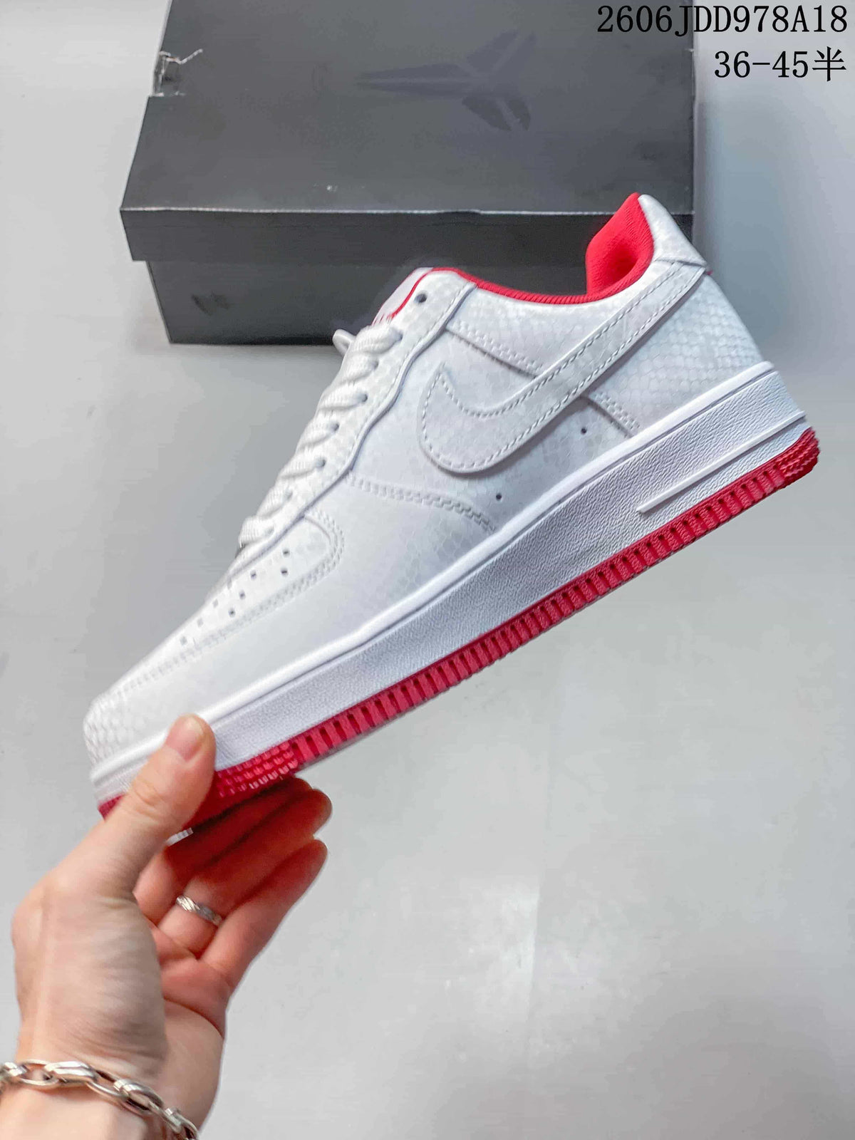 Side view of the white low-top sneaker with patterned panels, side logo, and red outsole.