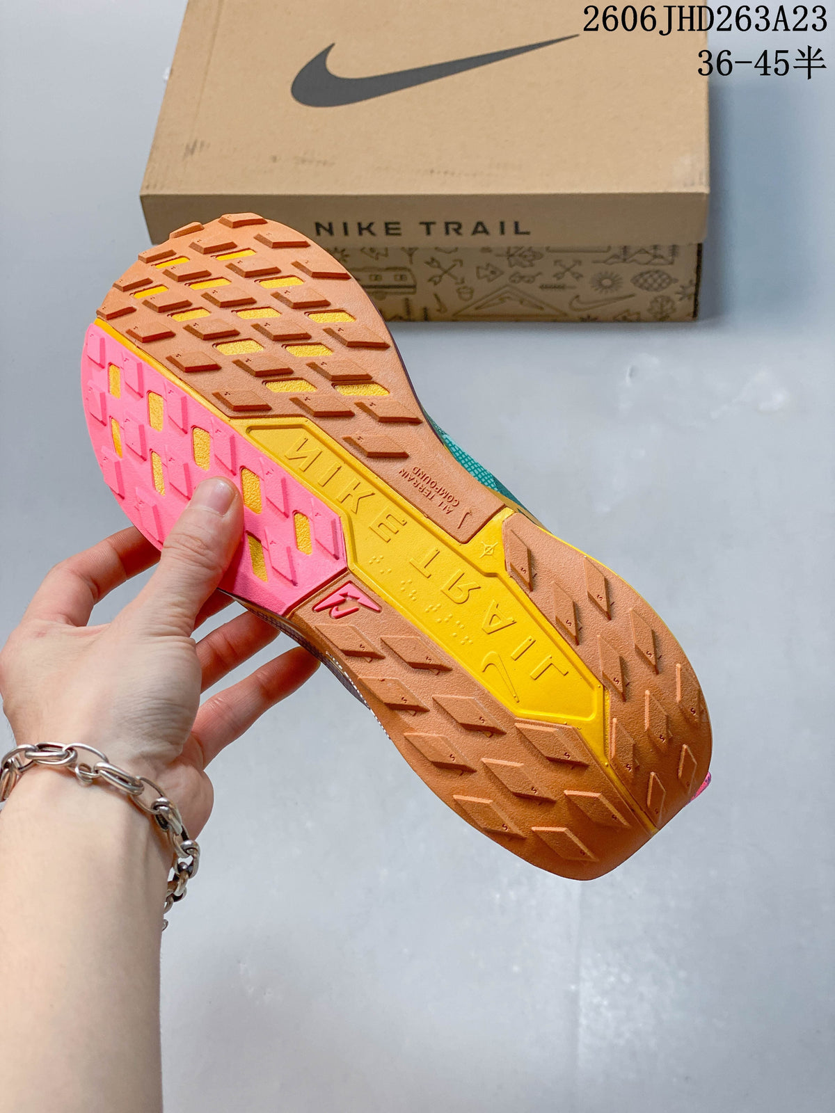 Lugged outsole of the Nike Pegasus Trail 5 shoe, shown in brown, pink, and yellow.