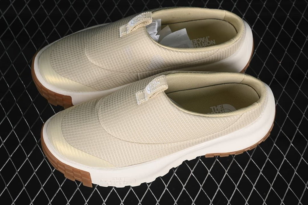 Pair of light neutral slip-on mule sneakers shown from above at an angle.