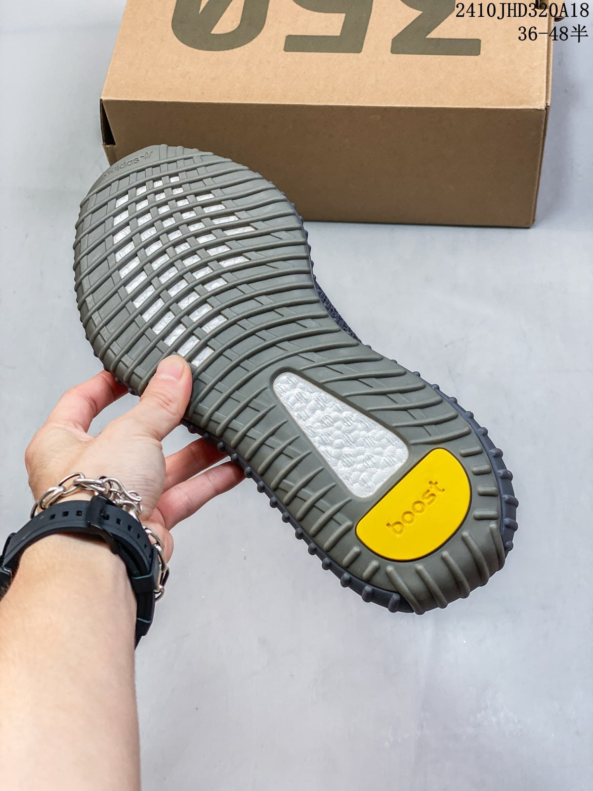 Underside of a sneaker showing a gray ribbed sole and yellow heel accent