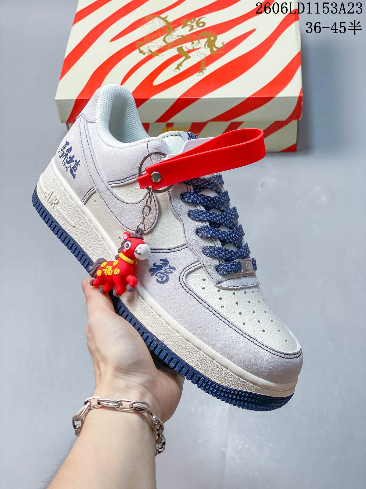 Angled view of a white and pale gray low-top sneaker with a red charm and dark blue accents