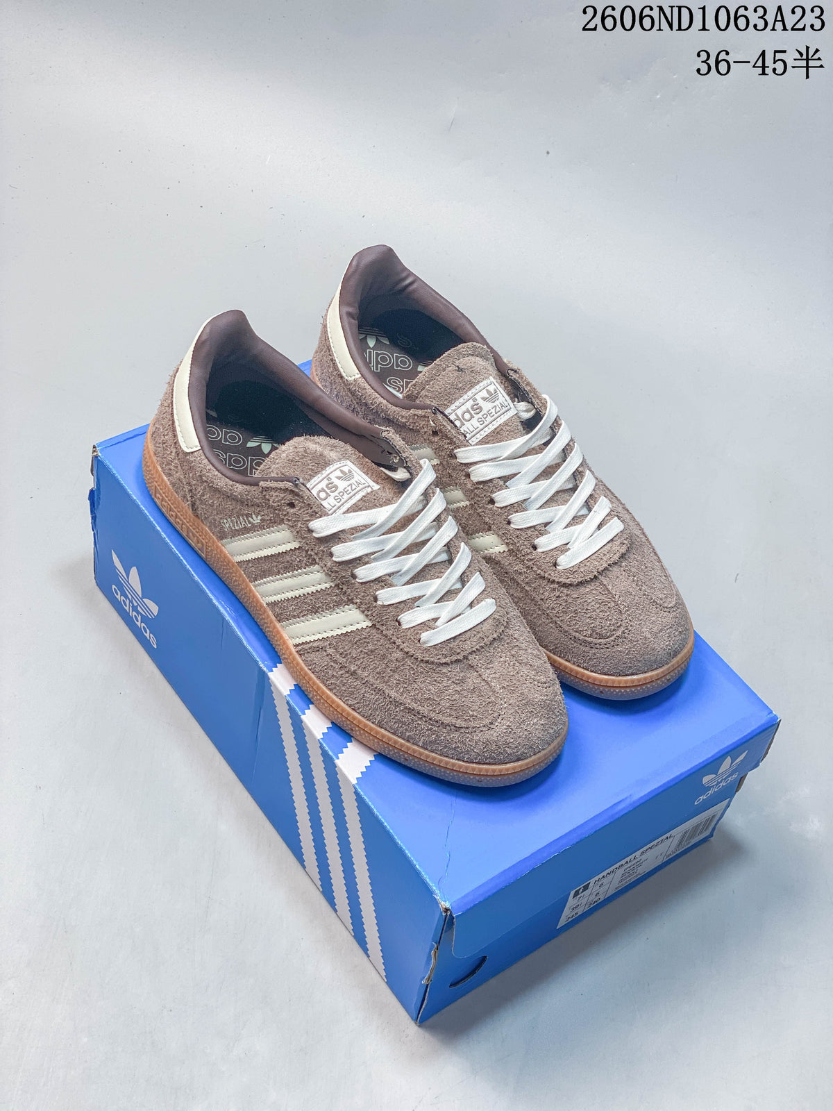Pair of taupe Adidas Spezial low-top sneakers with off-white stripes and gum-colored soles on a blue Adidas box.