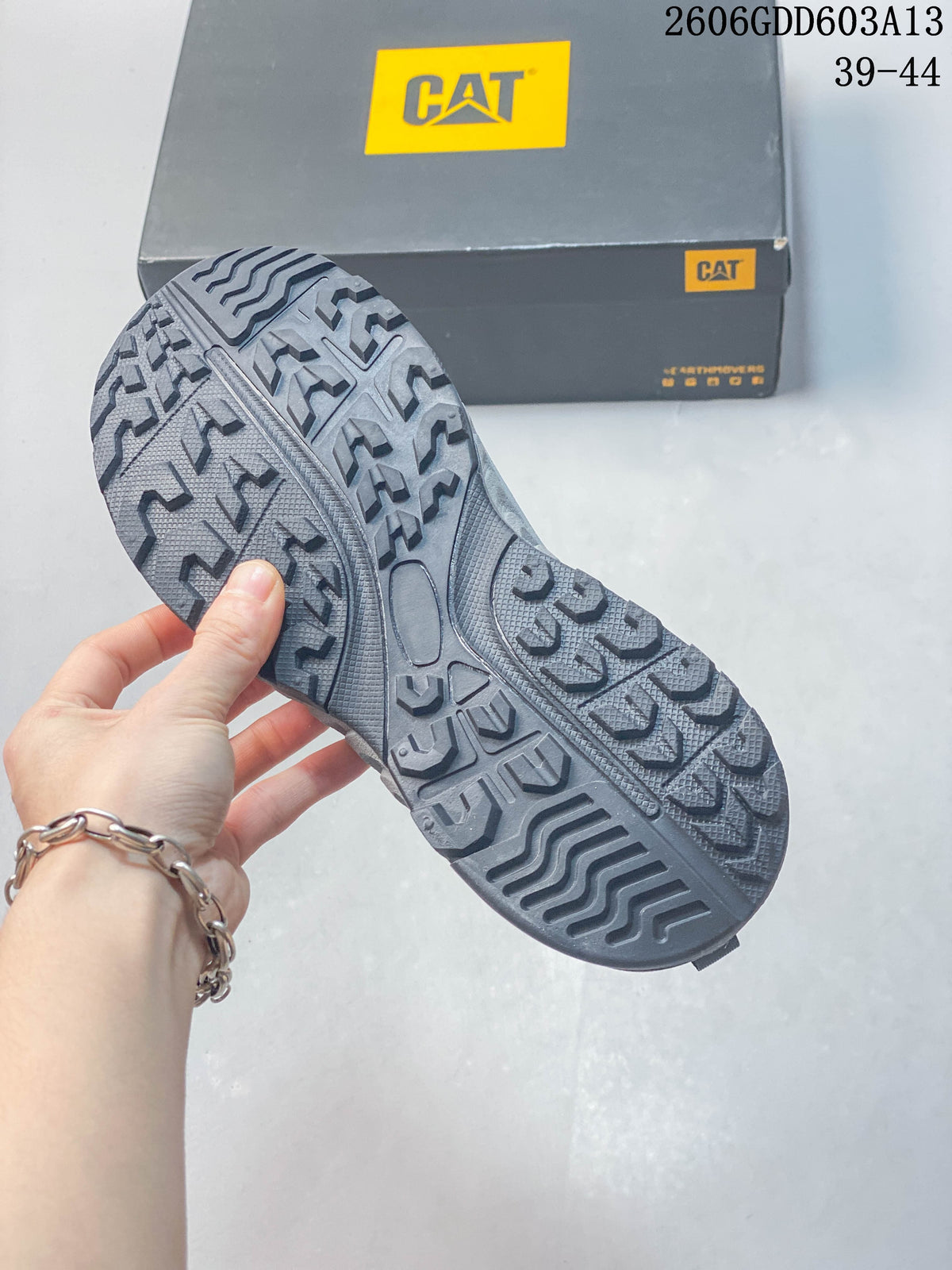 Close view of the sneaker's patterned dark gray outsole and CAT shoe box