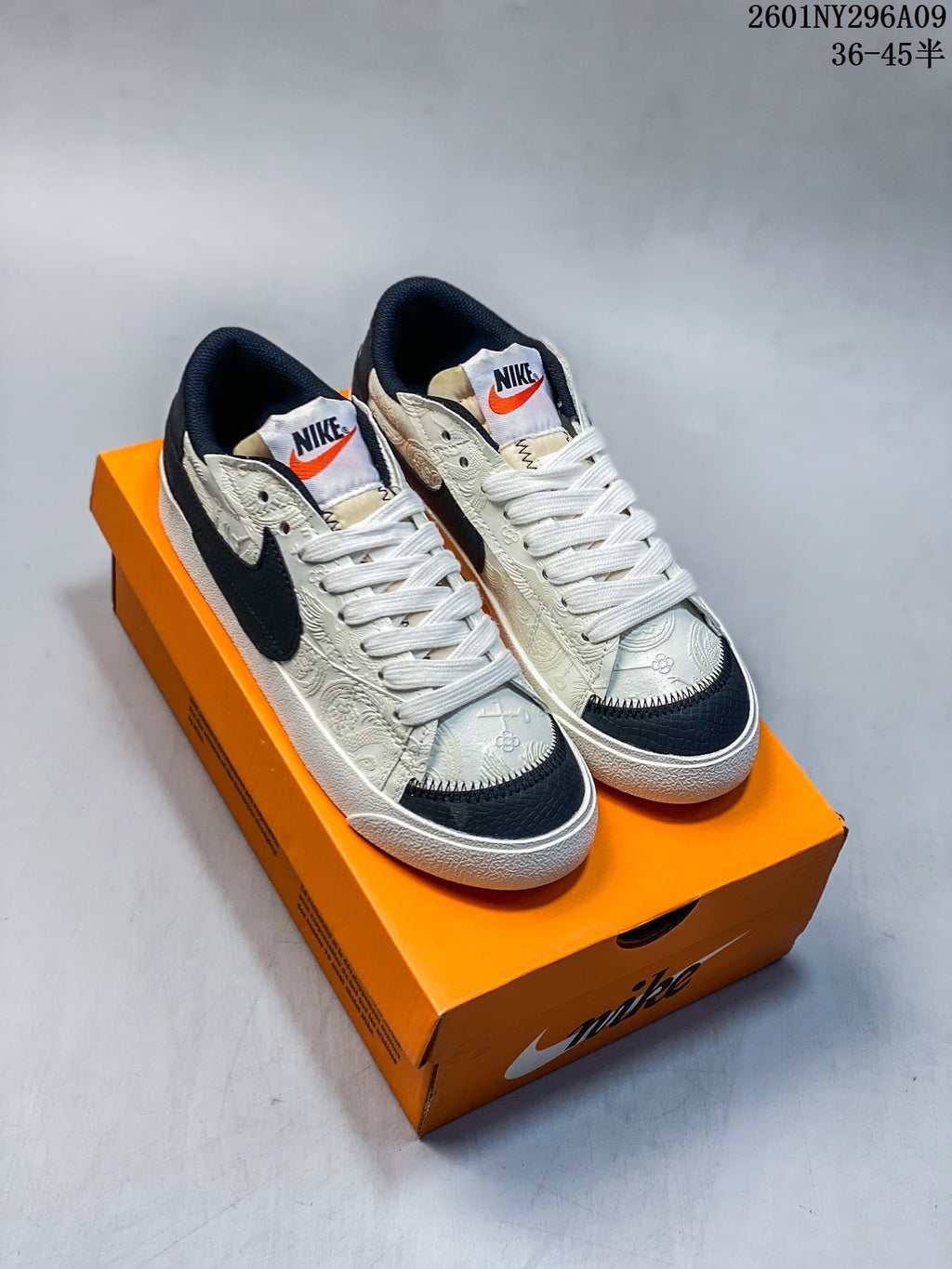 Pair of cream-patterned Nike Blazer Low '77 Jumbo-style sneakers with black accents and white laces on an orange shoe box