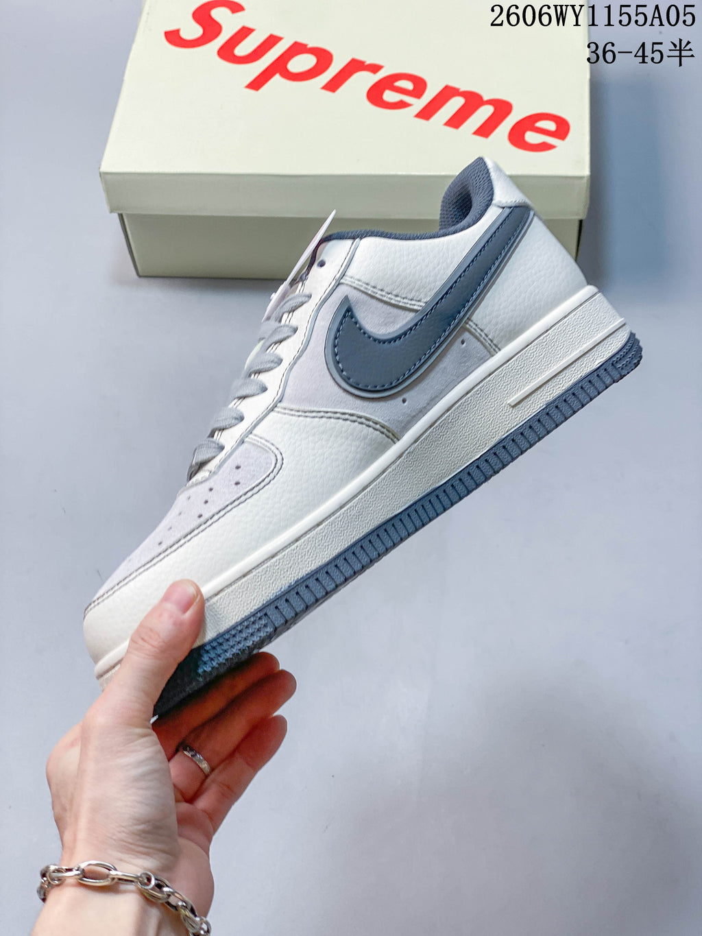 Side view of a white low-top sneaker with slate-blue accents and Supreme branding
