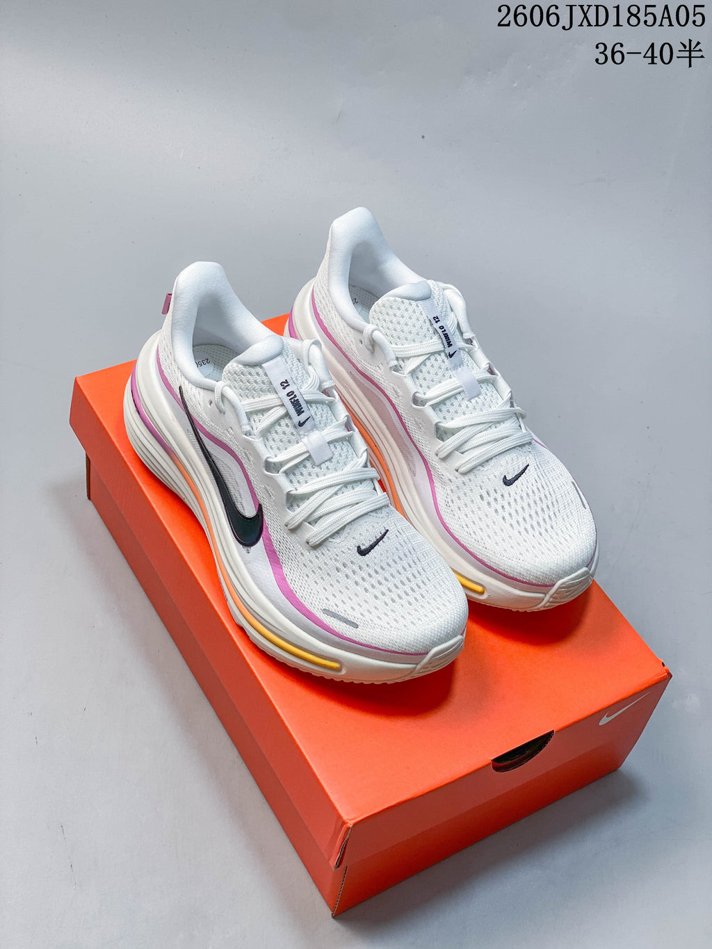 Pair of white Nike Winflo 12 running shoes with pink and orange accents, displayed on an orange box.