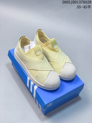 Pair of pale yellow slip-on shoes with crossed straps on a blue shoe box.