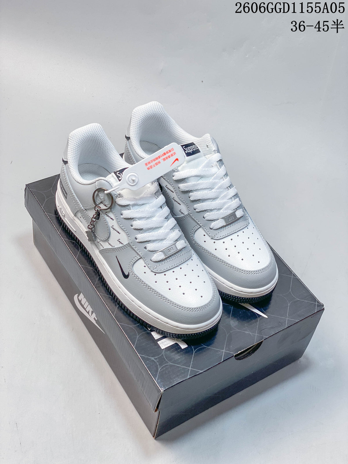 Pair of gray and white low-top Nike Air Force 1 sneakers with Supreme lettering and a decorative metal charm