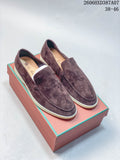 Pair of brown-toned slip-on loafers with apron toes and light-colored soles, shown on a box.
