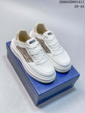 Pair of white Dior-branded sneakers with beige patterned side panels on a blue box.
