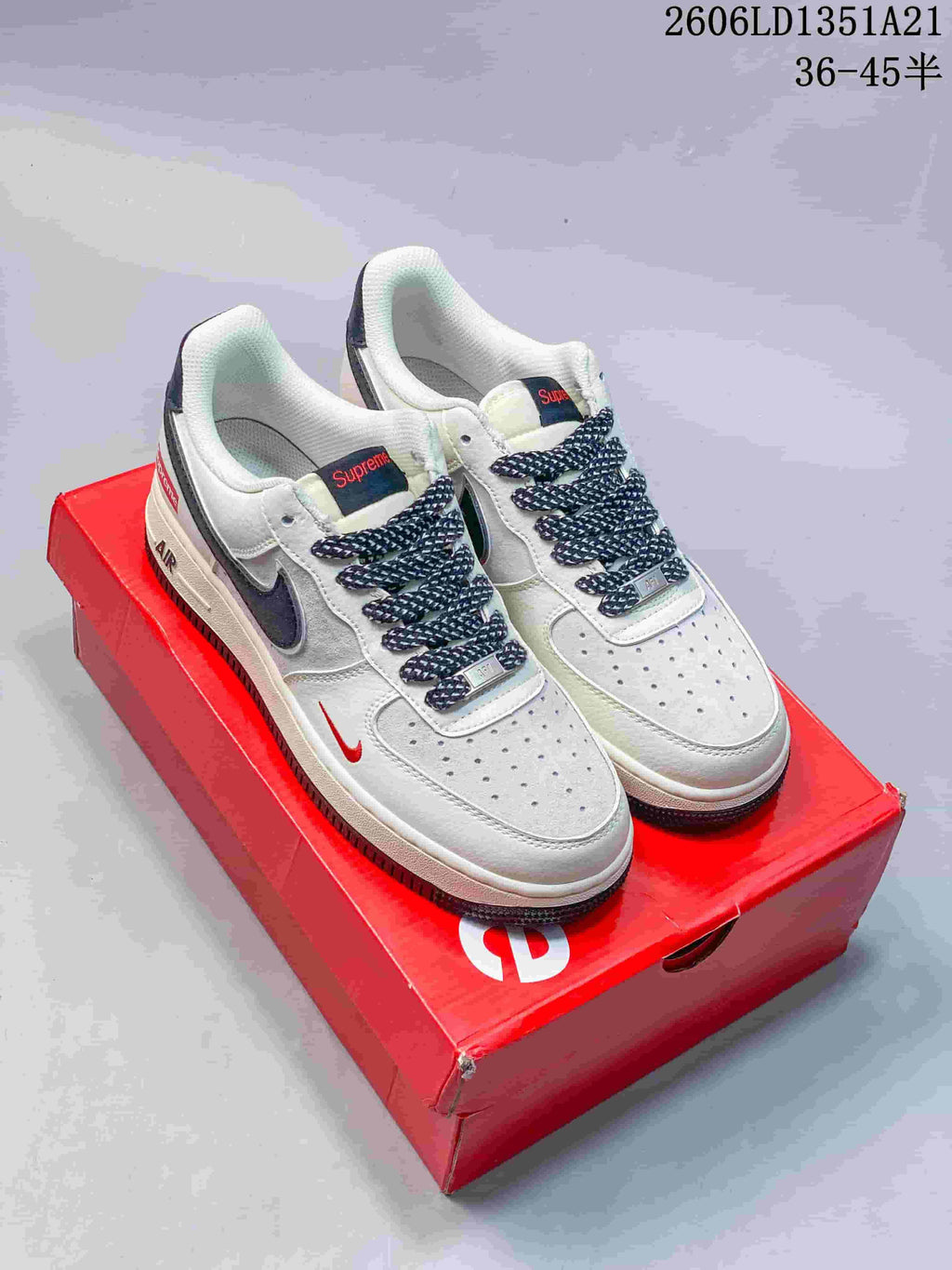 Pair of white low-top sneakers with dark Swooshes, patterned laces, red accents, and a red box.