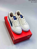 Pair of cream PUMA low-top sneakers with navy and burgundy accents, shown on a red shoebox.