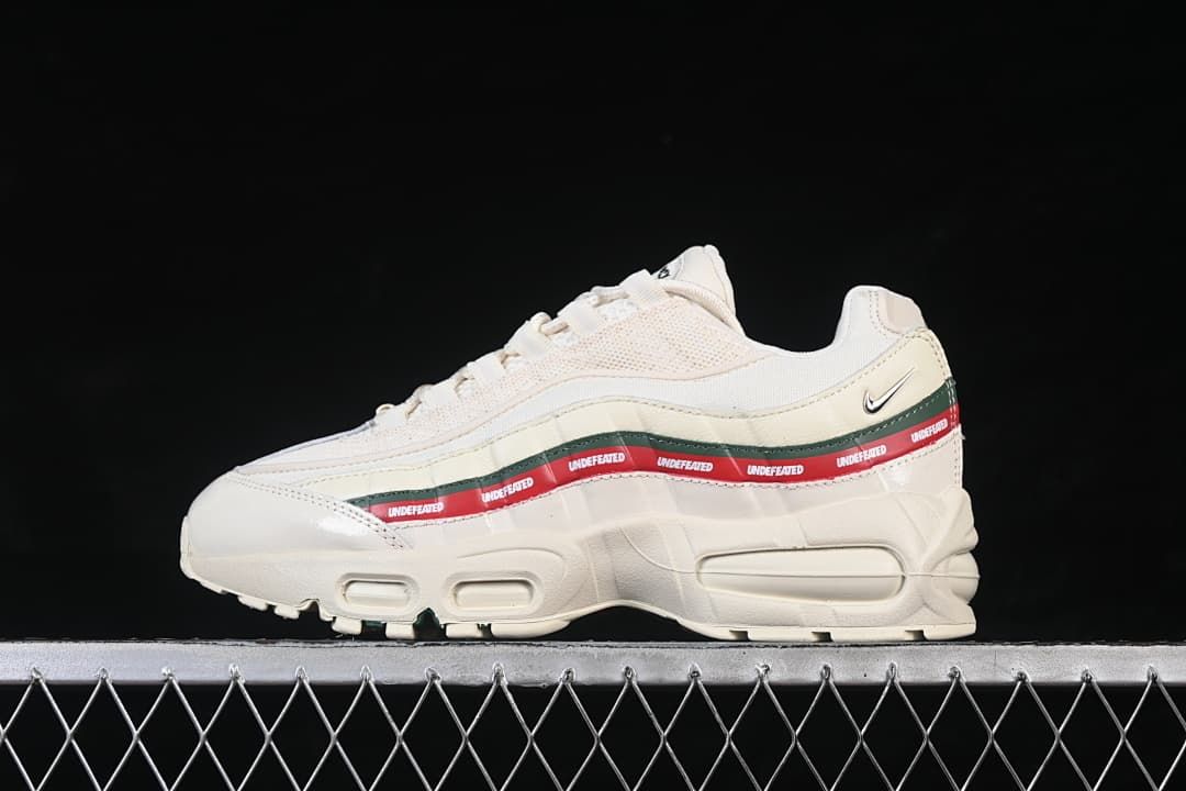 Side view of an off-white Nike Air Max 95 SP x Undefeated sneaker with green and red side accents.