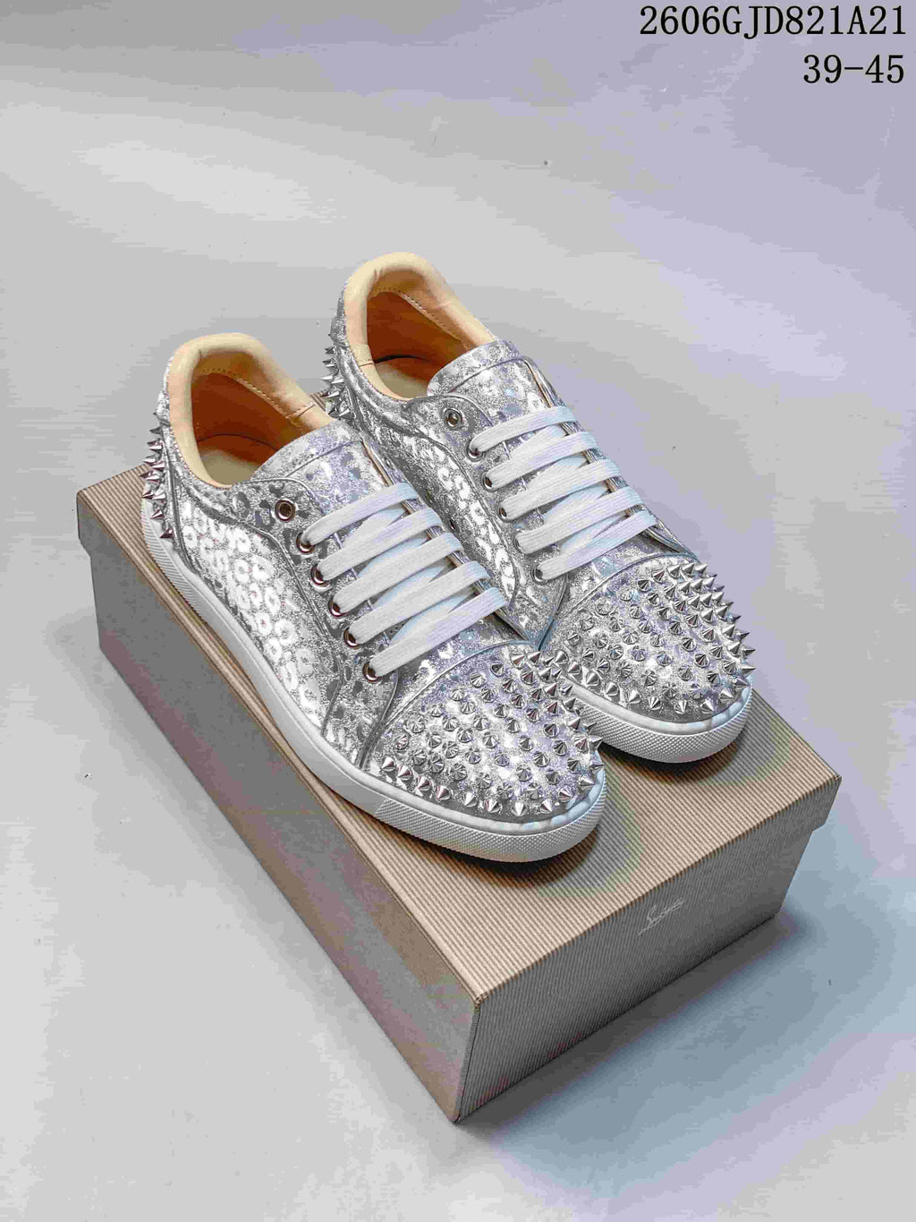 Pair of silver patterned low-top sneakers with metallic studs, white laces, and red soles