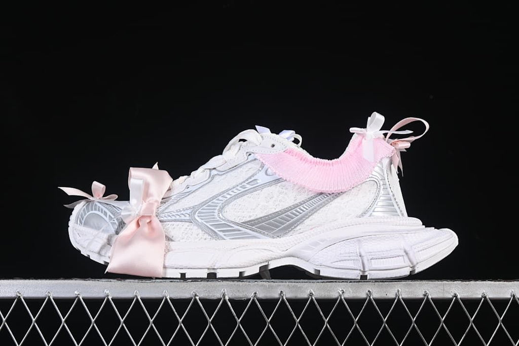 Side view of white Balenciaga 3XL-style sneakers with silver-toned details, pink trim, and ribbon bows.