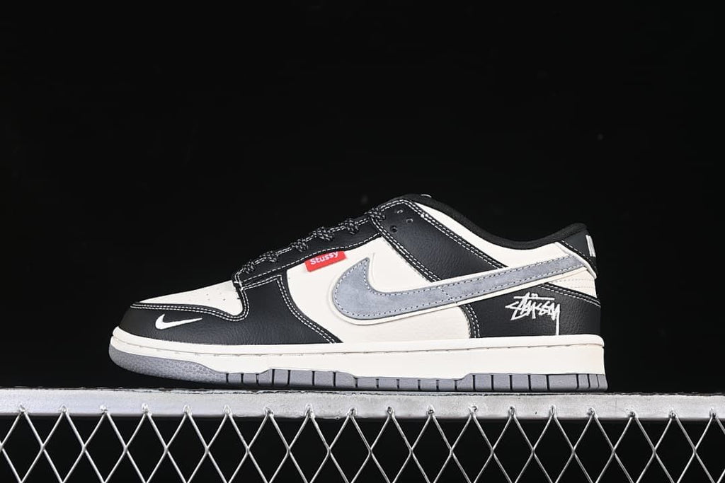 Side view of a black, white, and grey Nike SB Dunk Low with Stüssy details